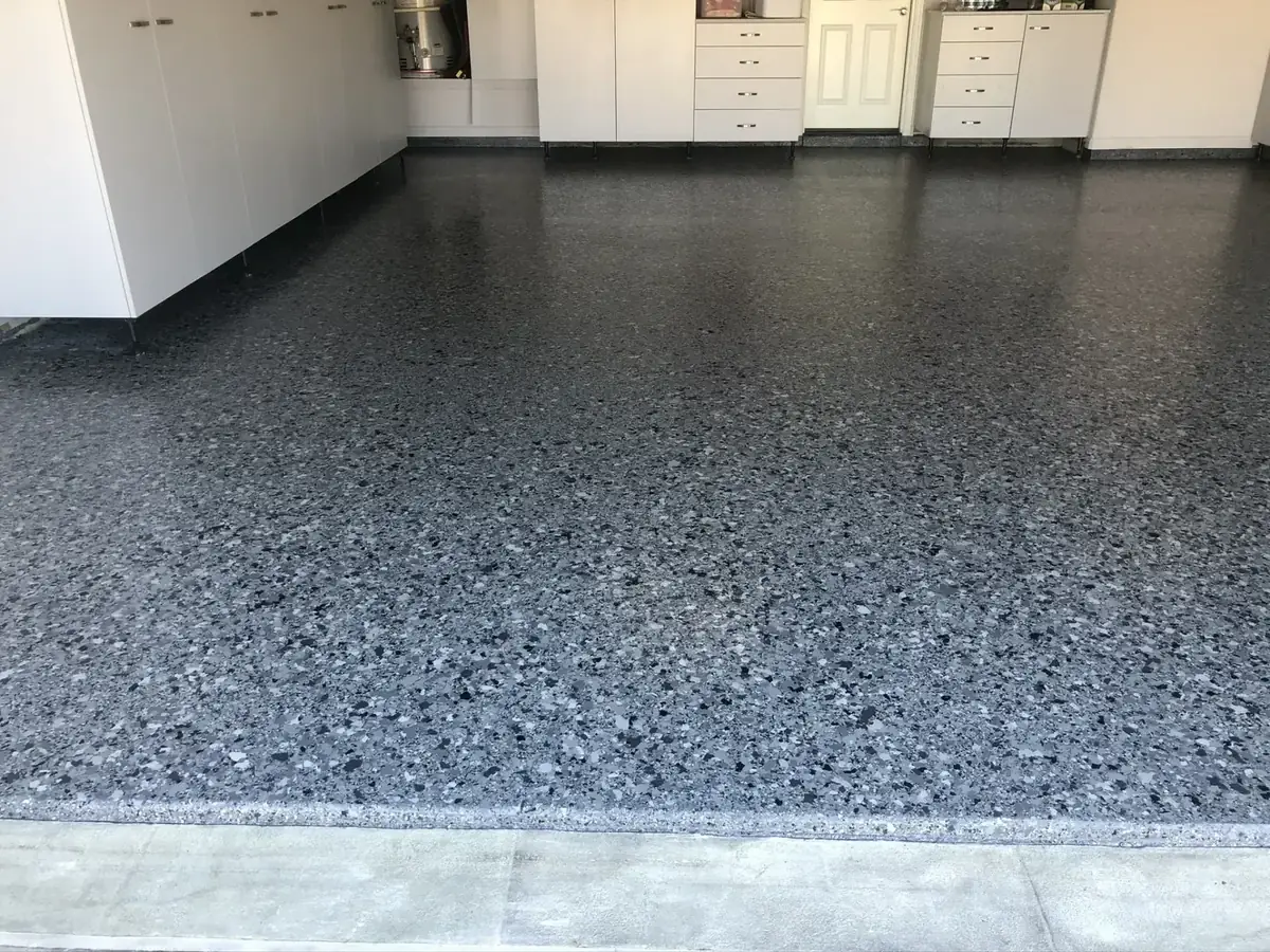 A garage with a gray concrete floor and white cabinets.