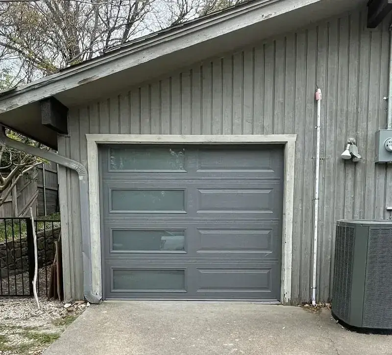A gray garage door with a gray air conditioner next to it